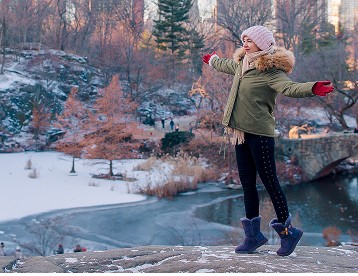 Top view of a hill with a frozen lake below it. There is a woman with her arms spread on the top of the hill