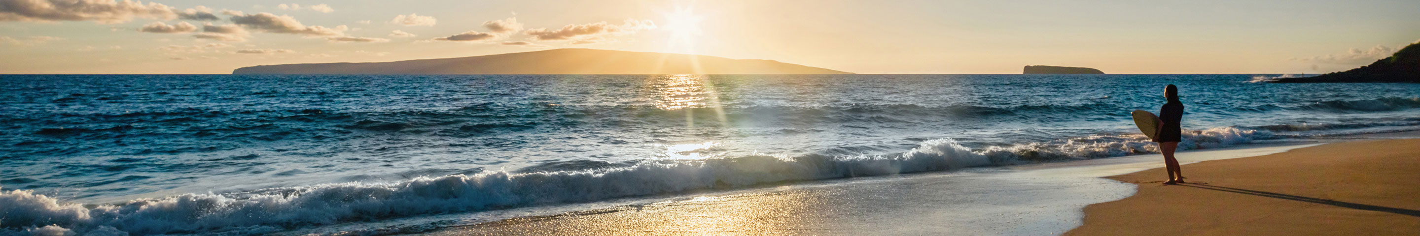 A sunny island getaway, with a person holding a surfboard on the shoreline.